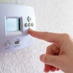 Man's finger pressing a wall-mounted electronic thermostat button.