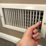 A hand using the lever on a heating register to open the vent.