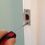 Man's hand screwing a door jamb's strike plate.