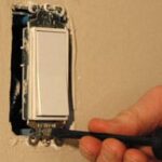 Man's fingers screwing a light switch into a mounting slot.