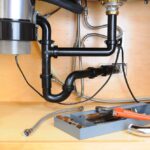 Kitchen plumbing system beneath a sink, including disposer and joined piping.